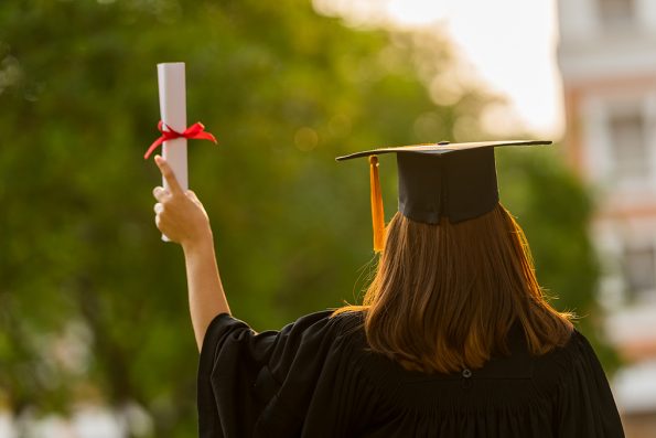 Female graduate of a university wearing a cap and gown and holding up a diploma