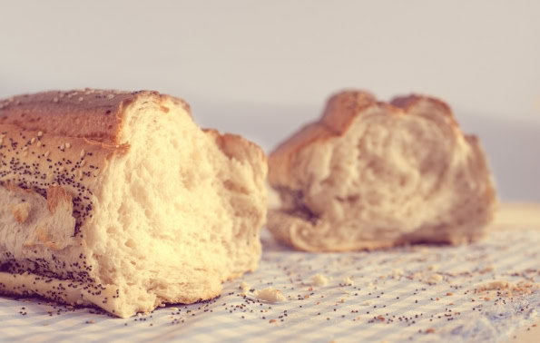 A loaf of bread torn in half, with crumbs littering the table surface