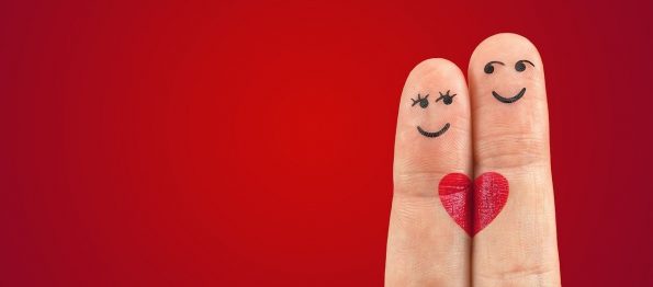 Two fingers with faces doodled on the tip and a heart drawn where the two touch