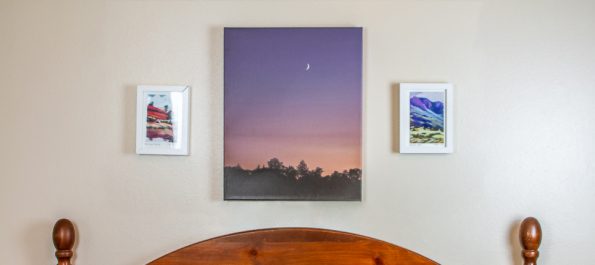 Photo of a moon rising over trees printed on an art canvas, hanging over a bed between two smaller framed images